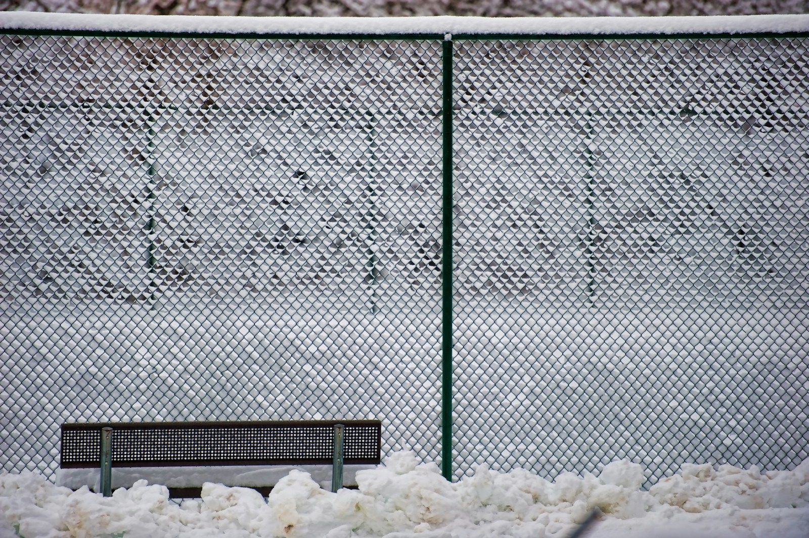 A bench sitting in the snow next to a fence